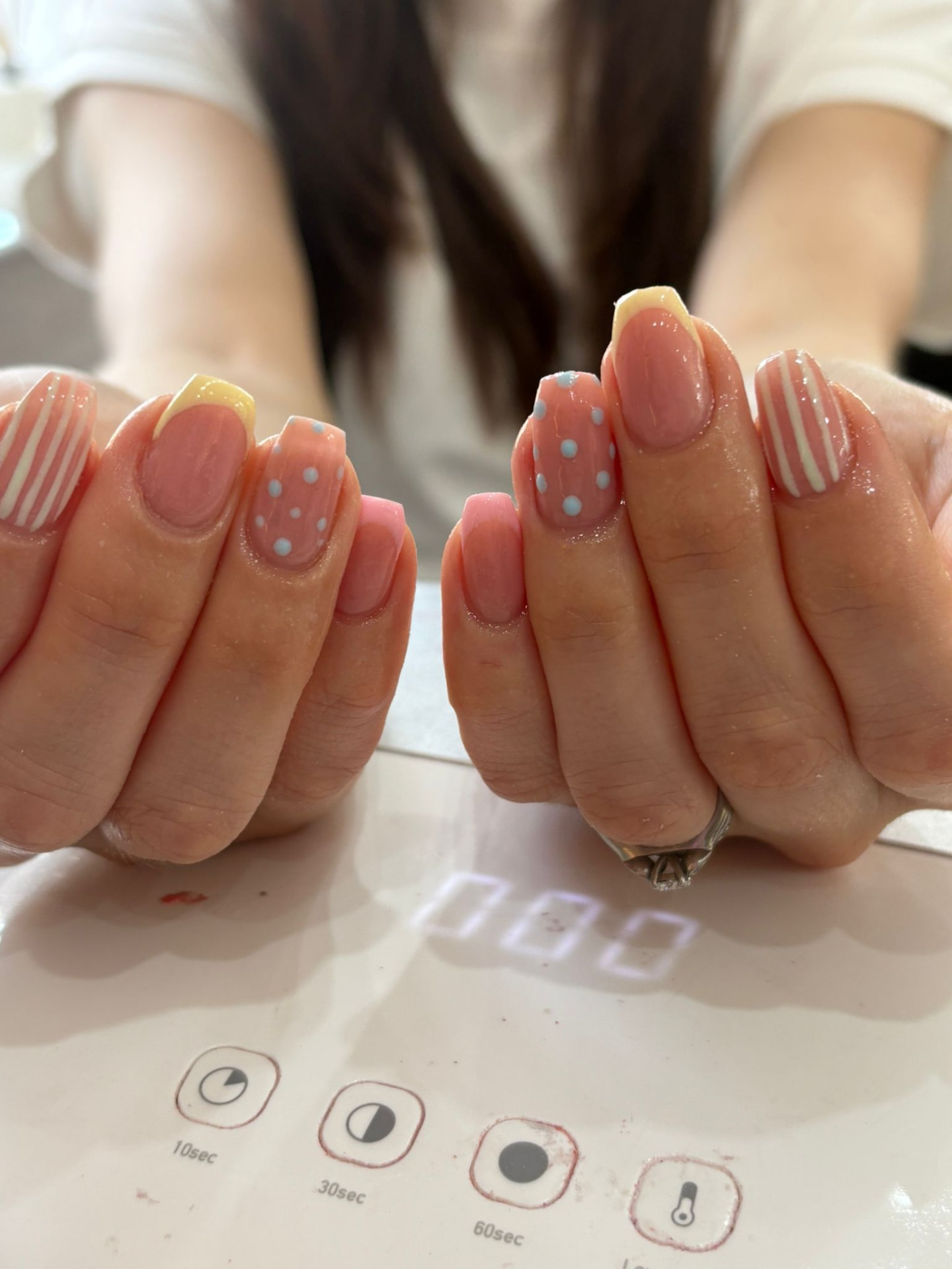 Hand-painted nail art with stripes, polka dots and yellow tips curing under a nail lamp