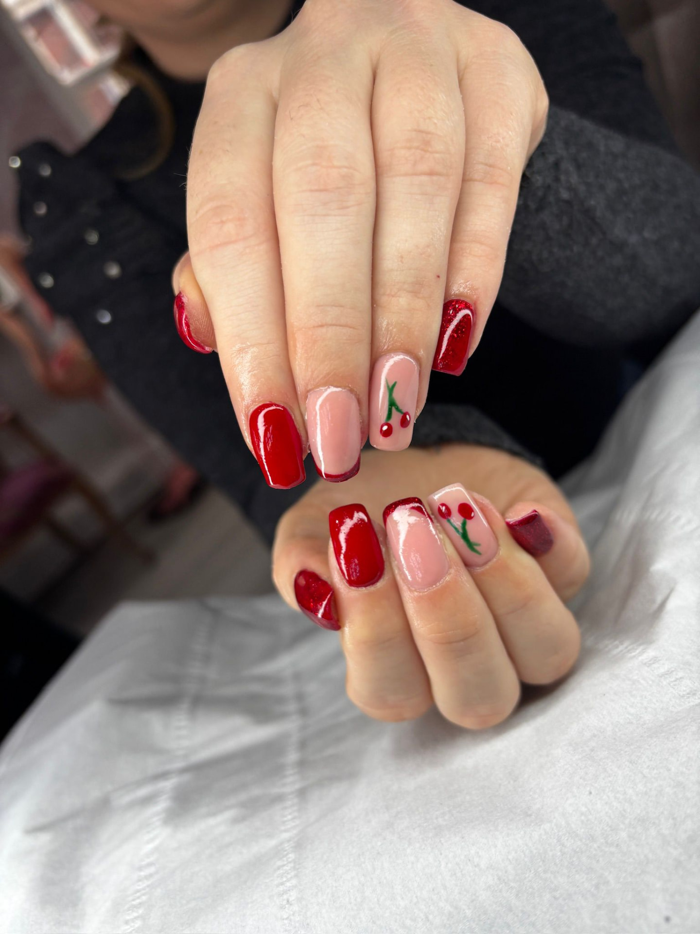 Red and cherry-themed nail art with French tips and glitter accents